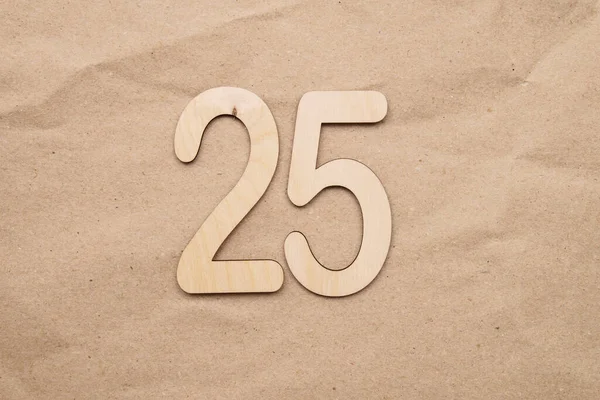 Light wooden numbers 25 lie on craft paper in the center