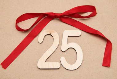 Hafif ahşap numaralar. 25 numara. Ortasında kırmızı bir fiyonk olan el işi kağıtlarının üzerinde yatıyor.