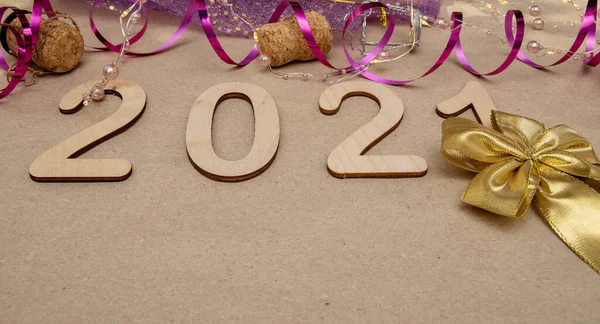 Light wooden numbers 2021 lie in the center on craft paper with packing tape, champagne corks, gold bow