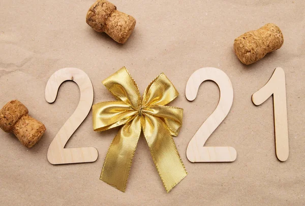 Light wooden 2021 numbers lie in the center on craft paper with gold bow and champagne corks