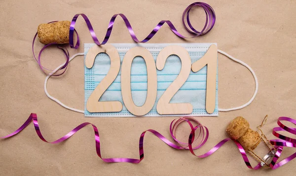 ight wooden numbers 2021 lie in the center on a medical disposable blue mask on craft paper with champagne corks and packing tape