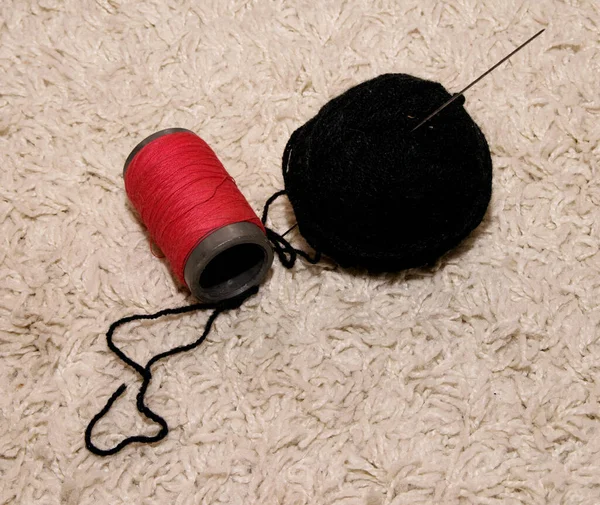 白い背景に黒い編み針と赤い糸のスプールを持つウールのボールが横たわっています — ストック写真