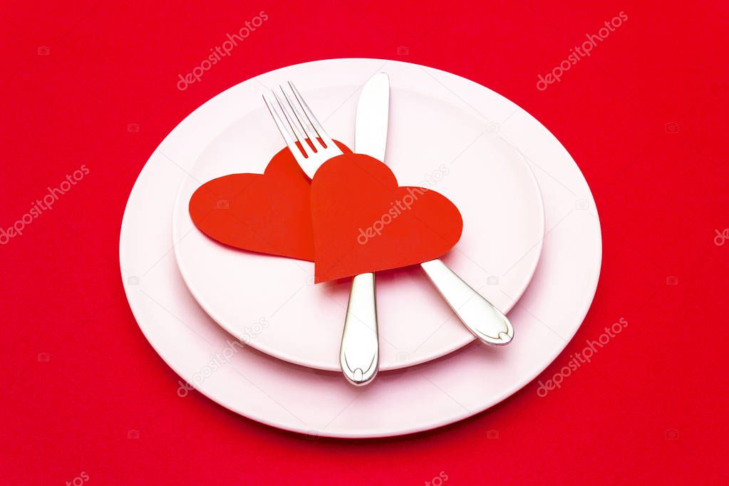 Valentines day (or wedding) set with fork and knife, paper hearts on red background.