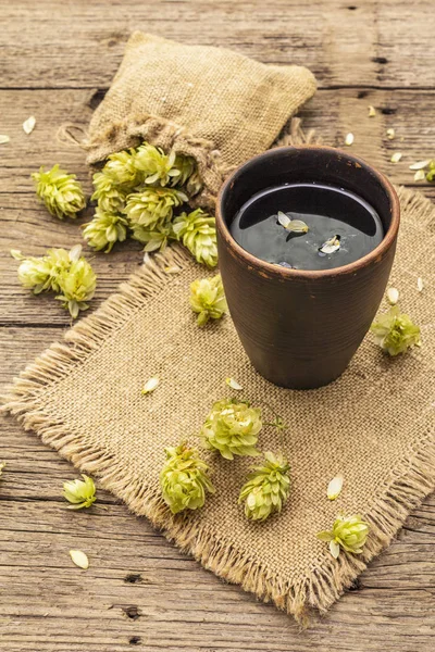 Tasse beruhigenden Kräutertee mit frischem Wildhopfen. Hopfenzapfen im Sack auf Vintage-Brettern Hintergrund — Stockfoto