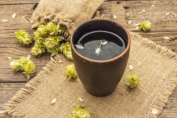 Чашка успокаивающего травяного чая со свежим диким хмелем. Конусы хмеля в мешке на фоне старинных досок — стоковое фото