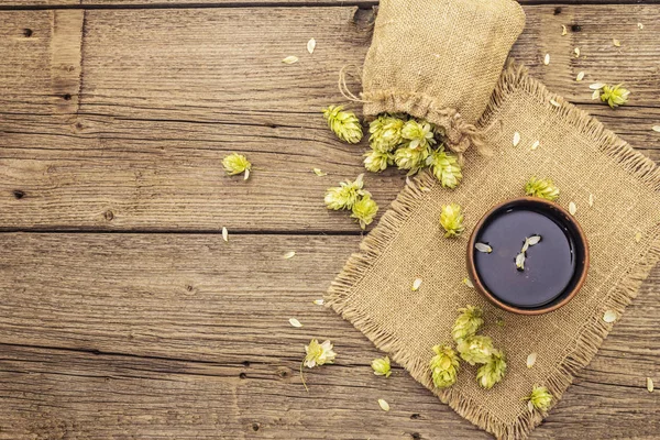 Tasse beruhigenden Kräutertee mit frischem Wildhopfen. Hopfenzapfen im Sack auf Vintage-Brettern Hintergrund — Stockfoto