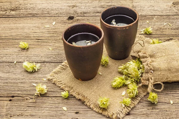 Tasse beruhigenden Kräutertee mit frischem Wildhopfen. Hopfenzapfen im Sack auf Vintage-Brettern Hintergrund — Stockfoto