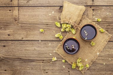 Taze yabani zıpzıp ile bir fincan sakinleştirici bitki çayı. Eski tahta arka planda çuval içinde kozalaklar