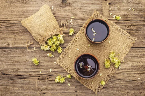 Чашка успокаивающего травяного чая со свежим диким хмелем. Конусы хмеля в мешке на фоне старинных досок — стоковое фото