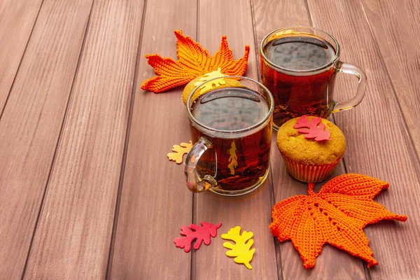 Hot autumn drink. Black tea with cupcakes, colorful leaves