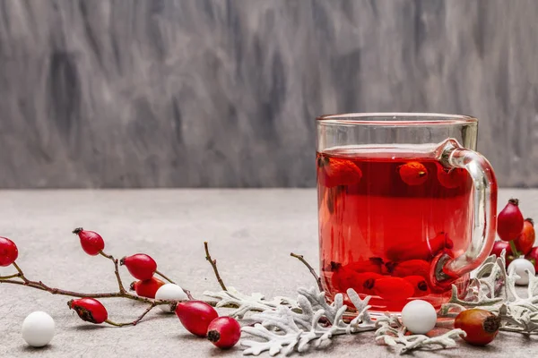 Hot dog-rose tea. Winter drink for good mood with fresh berries, leaves and candies. Stone concrete background — Stock Photo, Image