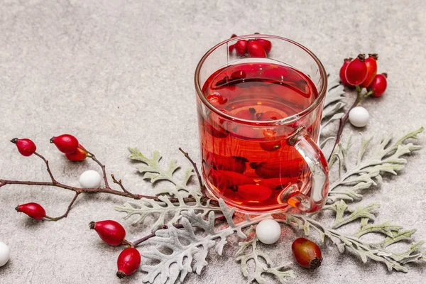 Чай из роз хот-догов. Зимний напиток для хорошего настроения со свежими ягодами, листьями и конфетами. Каменный бетон — стоковое фото