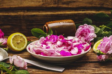 Gül yaprakları reçeli pişirmek için gerekli malzemeler. Şeker, limon, mis kokulu çiçekler. Eski tahta masa.