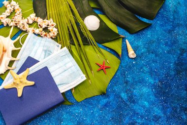 Seyahat ve tatil Coronavirüs konsepti. 2020 yazında tıbbi maske, pasaport, plaj kıyafeti, deniz sembolleri ve takılarla donatılmış. Deniz arkaplanı