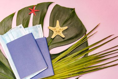 Seyahat ve tatil Coronavirüs konsepti. 2020 yazında tıbbi maske, pasaport, plaj kıyafeti, deniz sembolleri ve takılarla donatılmış. Yumuşak pembe arkaplan