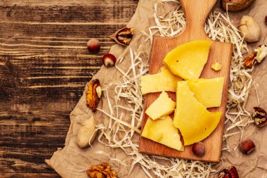 Yıllanmış Gouda peyniri parçaları. Ceviz, ceviz ve fındık. Kesme tahtası, eski ahşap masa, üst manzara.