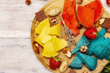 Peynir tabağı. Çeşitli renkte sert Hollanda peynirleri. Mavi ve kırmızı pesto, yıllanmış gouda. Çilek, çikolata, fındık, bitki ve çiçek. Beyaz tahta tahta arka plan, üst görünüm