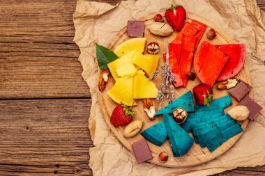 Peynir tabağı. Çeşitli renkte sert Hollanda peynirleri. Mavi ve kırmızı pesto, yıllanmış gouda. Çilek, çikolata, fındık, bitki ve çiçek. Eski tahta arka plan, üst görünüm
