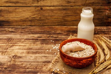 Vejetaryen yulaf sütü, sütsüz süt. Seramik kasede kurumuş gevrek, cam şişe, yulaf. Vintage ahşap arkaplan, kopyalama alanı