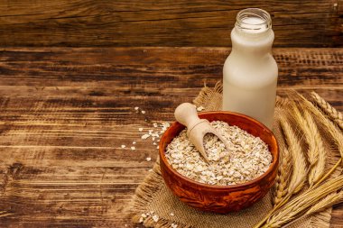 Vejetaryen yulaf sütü, sütsüz süt. Seramik kasede kurumuş gevrek, cam şişe, yulaf. Vintage ahşap arkaplan, kopyalama alanı