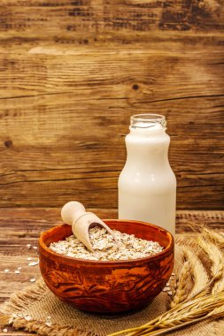 Vejetaryen yulaf sütü, sütsüz süt. Seramik kasede kurumuş gevrek, cam şişe, yulaf. Vintage ahşap arkaplan, kopyalama alanı