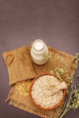 Vejetaryen yulaf sütü, sütsüz süt. Seramik kasede kurumuş gevrek, cam şişe, yulaf. Siyah taş arkaplan, üst görünüm