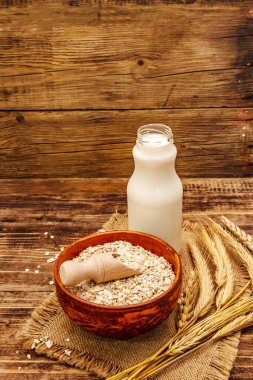 Vejetaryen yulaf sütü, sütsüz süt. Seramik kasede kurumuş gevrek, cam şişe, yulaf. Vintage ahşap arkaplan, kopyalama alanı