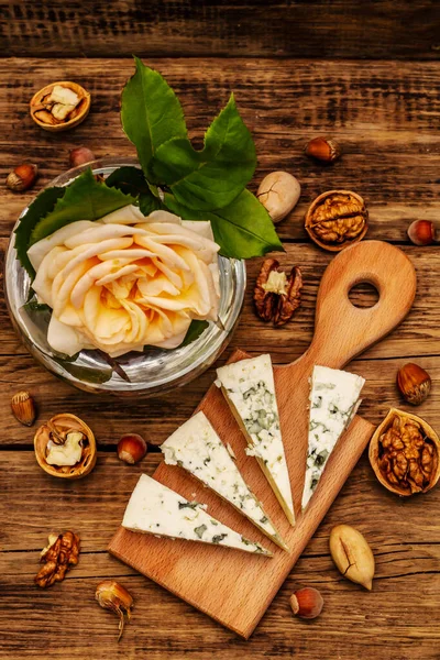 Cheese with blue mold. Ingredient for a cheese plate. Nuts, fragrant bay leaves, knife. Vintage wooden boards background, close up