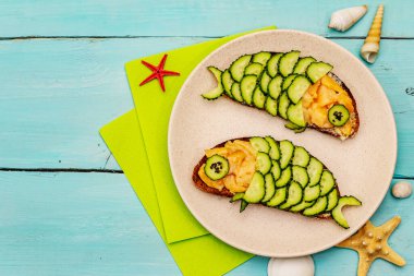 Çocuklar için salatalıklı komik somon sandviçleri. Sağlıklı öğle yemeği, turkuaz tahta arka plan