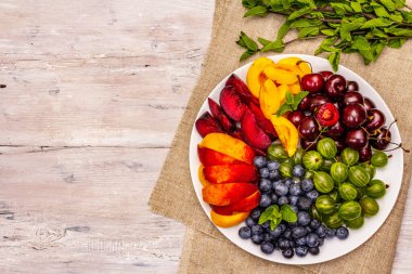 Tabakta çeşitli taze meyveler. Vişne, Bektaşi üzümü, yabanmersini, şeftali dilimleri, erik ve kayısı, kokulu nane. Tahta kaplama arka plan, üst görünüm