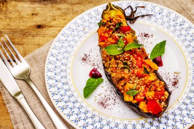 Karniyarik geleneksel Türk yemekleri. Kıyma, domates, yeşillik ve susamlı patlıcan dolması. Tabak eski ahşap bir masada servis edildi, yakın çekim.