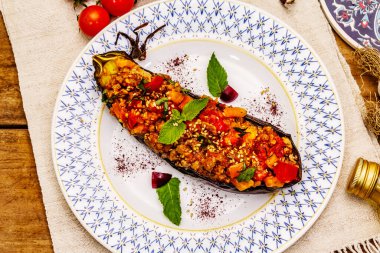 Karniyarik geleneksel Türk yemekleri. Kıyma, domates, yeşillik ve susamlı patlıcan dolması. Tabak eski ahşap bir masada servis edildi.