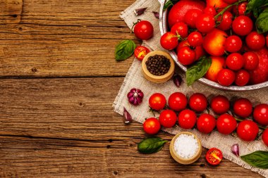 Olgun domates hasadı. Farklı renkte meyveler, taze sarımsak, taze fesleğen yaprağı, tuz ve baharatlar. Eski ahşap zemin, üst manzara