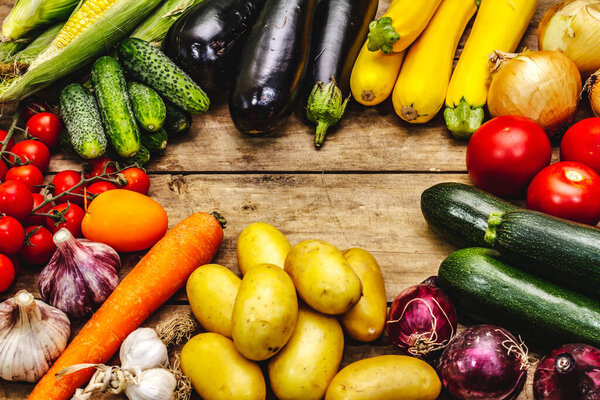 Harvest a variety of ripe vegetables. Fresh cucumbers, tomatoes, eggplants, zucchini, onions, garlic, potatoes, carrots. Old wooden boards background, place for text, close up