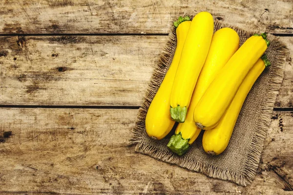 Whole unpeeled yellow zucchini. New harvest, on sackcloth, wooden boards background, top view