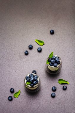 Yabanmersini ve chia tohumlu yoğurt. Sağlıklı ve yararlı kahvaltı konsepti. Olgun böğürtlen, nane yaprağı, siyah taş beton arka plan, üst manzara