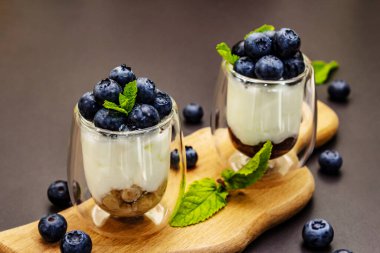 Yaban mersinli yoğurt ve tahta kesme tahtasında chia tohumu. Sağlıklı ve yararlı kahvaltı konsepti. Olgun böğürtlen, nane yaprağı, siyah taş beton arka plan, kapat