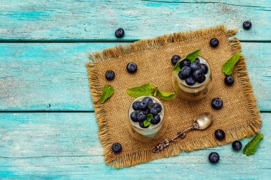 Yabanmersini ve chia tohumlu yoğurt. Sağlıklı ve yararlı kahvaltı konsepti. Olgun böğürtlenler, nane yaprakları, trend turkuaz ahşap arka planda gümüş kaşık, üst manzara