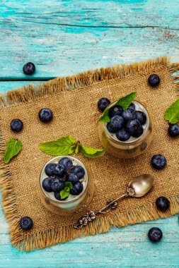Yabanmersini ve chia tohumlu yoğurt. Sağlıklı ve yararlı kahvaltı konsepti. Olgun böğürtlenler, nane yaprakları, trend turkuaz ahşap arka planda gümüş kaşık, üst manzara