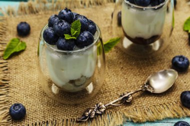 Yabanmersini ve chia tohumlu yoğurt. Sağlıklı ve yararlı kahvaltı konsepti. Olgun böğürtlen, nane yaprağı, trend turkuaz ahşap arka planda gümüş kaşık, kapat