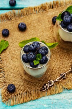 Yabanmersini ve chia tohumlu yoğurt. Sağlıklı ve yararlı kahvaltı konsepti. Olgun böğürtlenler, nane yaprakları, trend turkuaz ahşap arka planda gümüş kaşık, üst manzara