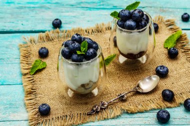 Yabanmersini ve chia tohumlu yoğurt. Sağlıklı ve yararlı kahvaltı konsepti. Olgun böğürtlen, nane yaprağı, trend turkuaz ahşap tahta arka planda gümüş kaşık, kopyalama alanı