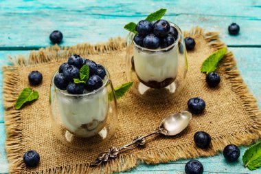 Yabanmersini ve chia tohumlu yoğurt. Sağlıklı ve yararlı kahvaltı konsepti. Olgun böğürtlen, nane yaprağı, trend turkuaz ahşap tahta arka planda gümüş kaşık, kopyalama alanı