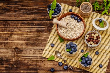 Sağlıklı ve yararlı kahvaltı konsepti. Yaban mersinli yoğurt, yulaf ezmesi ve chia çekirdeği. Olgun böğürtlen, nane yaprağı, tahta tahtada gümüş kaşık arka plan, üst manzara