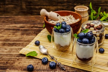 Sağlıklı ve yararlı kahvaltı konsepti. Yaban mersinli yoğurt, yulaf ezmesi ve chia çekirdeği. Olgun böğürtlenler, nane yaprakları, tahta tahtada gümüş kaşık arka plan, kopyalama alanı