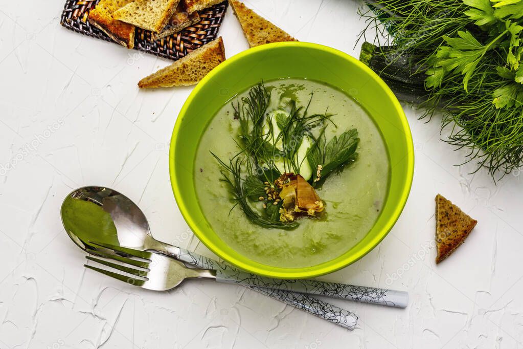 Green zucchini cream soup. Healthy vegan (vegetarian) food, crispy toast, sesame seeds, whole ripe fruits, fresh greens. White putty background, top view
