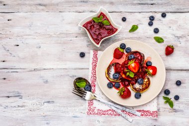 Taze böğürtlen ve çilek soslu süzme peynirli krep. Sağlıklı kahvaltı konsepti. Olgun yaban mersini, kokulu nane yaprakları, çatal bıçak takımı. Tahta kaplama arka plan, üst görünüm