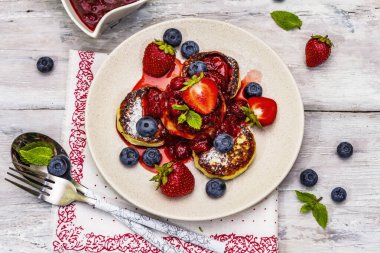 Taze böğürtlen ve çilek soslu süzme peynirli krep. Sağlıklı kahvaltı konsepti. Olgun yaban mersini, kokulu nane yaprakları, çatal bıçak takımı. Tahta kaplama arka plan, üst görünüm