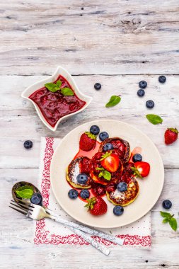 Taze böğürtlen ve çilek soslu süzme peynirli krep. Sağlıklı kahvaltı konsepti. Olgun yaban mersini, kokulu nane yaprakları, çatal bıçak takımı. Tahta kaplama arka plan, üst görünüm