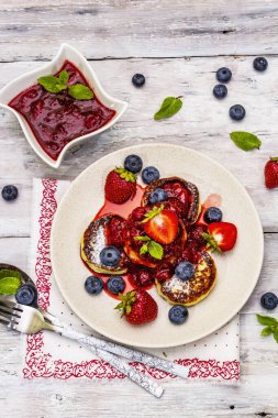 Taze böğürtlen ve çilek soslu süzme peynirli krep. Sağlıklı kahvaltı konsepti. Olgun yaban mersini, kokulu nane yaprakları, çatal bıçak takımı. Tahta kaplama arka plan, üst görünüm